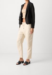 Černý blazer přes béžový crop top, spojený s krémovými kalhotami na šňůrku a černými sandály na blokovém podpatku s otevřenou špičkou.