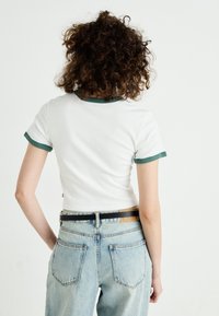 Vit bomullströja med grön ribbad krage och ärmslut, i kombination med ljusblå högmidjade denimjeans.