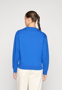 Felpa blu con maniche lunghe, scollatura rotonda e orlo a coste, realizzata in un tessuto morbido. Vista posteriore che mostra una texture morbida e cuciture.