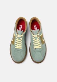 Gröna mockasneakers med gula snörning, bruna detaljer på sidorna och röda innersulor med vit "Camper"-logotyp. Platt gummisula.