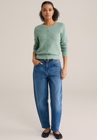 Mint zelena teksturirana jopica z gumbi, združena s svetlo modrimi kavbojkami z visokim pasom in črnimi balerinkami. Preprosta, priložnostna obleka.