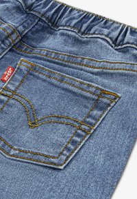 Μπλε ύφασμα τζιν με ελαστική μέση, επισημασμένο κέντημα σε κίτρινο και πίσω τσέπη με κλασικό κυρτό σχέδιο.