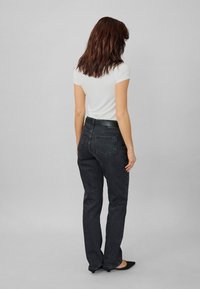 Jeans in denim nero con taglio dritto, vita alta e tasche posteriori, abbinati a una t-shirt bianca aderente e ballerine nere.