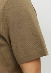 Chemise courte à manches courtes en tricot marron avec une texture côtelée. Présente un ourlet droit et une coupe ajustée au niveau de la couture de l'épaule.