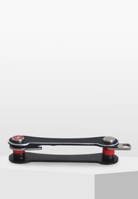 Zwart metalen multitool met rode rubberen accenten en zilveren hardware. Het ontwerp heeft een vlakke, verlengde vorm met ronde uiteinden.