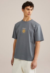Gray short-sleeve t-shirt with a round neckline. Front graphic features a yellow flower design within a square. Soft, smooth fabric.