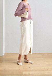 Maglione lavorato a maglia rosa chiaro, gonna bianca lungo caviglia con spacco laterale e scarpe flat beige con dettagli sulla fascia, abbinate a una borsa color crema.