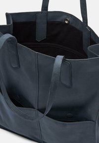 Borsa tote in pelle blu navy con texture morbida, apertura superiore, tasca interna e due manici robusti. Presenta un design minimalista e senza hardware visibile.