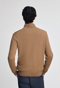 Brauner Wollpullover mit hohem Kragen, gerippten Bündchen und Saum, der eine glatte Textur aufweist. Die Rückansicht zeigt ein figuroptimiertes Design.
