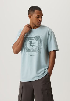 Jasnoniebieska koszulka bawełniana z centralnym graficznym wzorem, z akcentami w postaci drutu kolczastego oraz tekstem, z krótkimi rękawami i luźnym krojem.