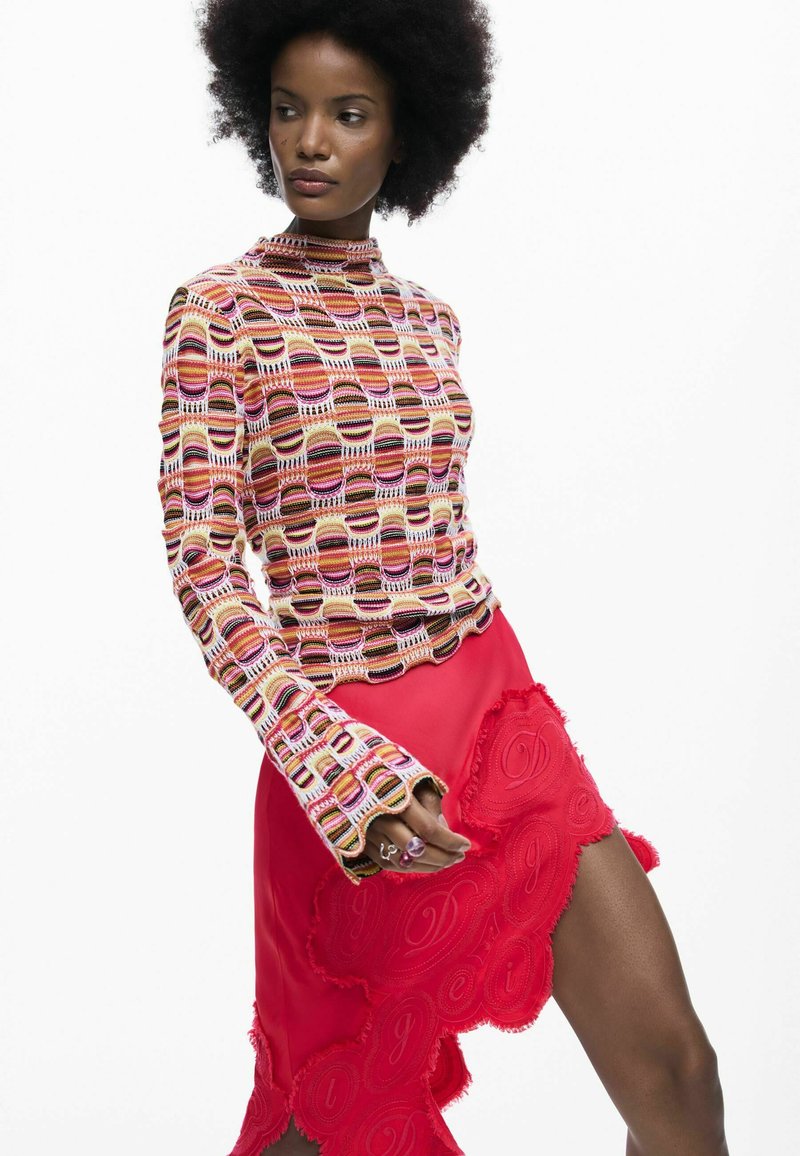 Dzianinowy top w kolorowe paski, z wysokim kołnierzem i rozszerzanymi rękawami, w połączeniu z czerwoną spódnicą z falującym brzegiem i haftowanymi detalami.