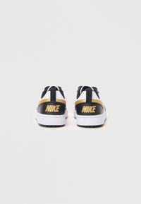 Une paire de baskets Nike noires, blanches et dorées vue de l'arrière, présentant le logo Nike sur le talon.