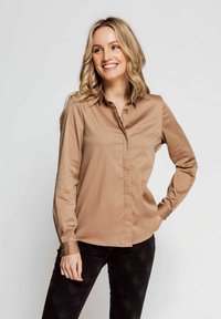 Light brown button-up shirt with a collar, long sleeves, and a smooth texture; paired with black textured pants.