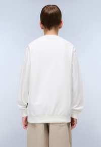 Sudadera blanca de cuello redondo con mangas largas, textura suave, puños y dobladillo acanalados, y una pequeña etiqueta de marca en un lado.