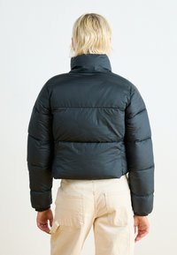 Svart boblejakke med høy krage, quiltet tekstur og kort design. Har elastiske mansjetter og en glatt, blank overflate.
