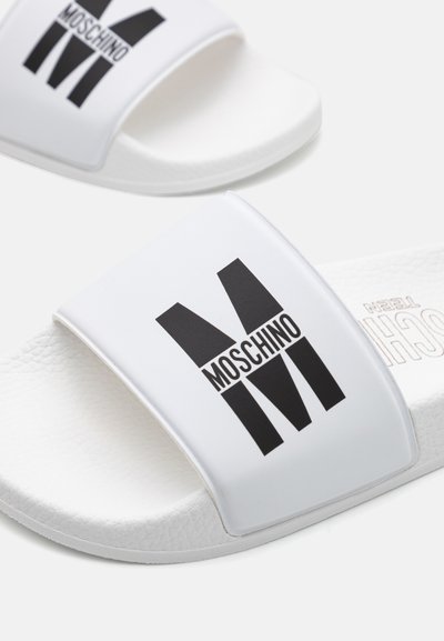 Sandales blanches à bande texturée avec un grand logo "M" noir. Semelle en caoutchouc lisse et design minimaliste.
