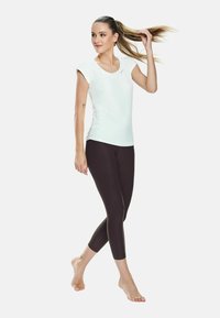 Top verde chiaro a maniche corte abbinato a leggings neri. Il top presenta un collo rotondo e un design aderente, mentre i leggings hanno una lunghezza cropped.