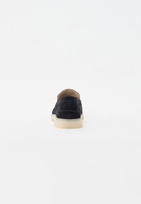 Marineblå semsket skinn slip-on sko med en jevn tekstur, uferdige kanter ved hælen, og en lett gummisåle. Baksidebilde mot en hvit bakgrunn.