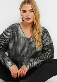 Schwarzer und silberner Pailletten-Pullover mit V-Ausschnitt und langen Ärmeln, der ein strukturiertes Muster und einen lockeren Schnitt aufweist. Kombiniert mit schwarzen Hosen.