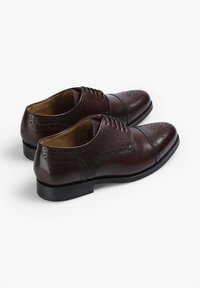 Zapatos de vestir de cuero burdeos oscuro con detalles de brogue, puntera redonda y cordones. Presentan una textura lisa y un tacón bajo negro.