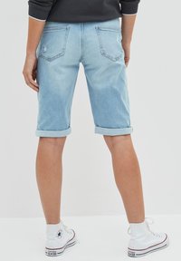 Vaaleansiniset farkkushortsit, joissa on käännetty helma, takataskut ja pieni kulutus. Yhdistetty valkoisiin korkeisiin tennareihin.