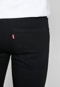 Svarta denimjeans med en bakficka som har ett böjt sömmönster och en liten röd Levi's-lapp på högra sidan.