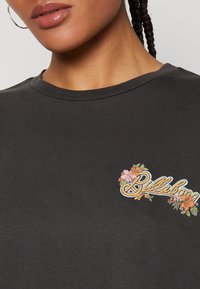 Μαύρο βαμβακερό μπλουζάκι με χρωματιστή κεντητή λουλουδάτη διακόσμηση στο αριστερό στήθος, με στρογγυλή λαιμόκοψη και κοντά μανίκια.