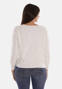 Maglione bianco a maglia con maniche raglan a tre quarti e scollo rotondo, abbinato a jeans in denim blu scuro. Texture morbida, vestibilità casual.