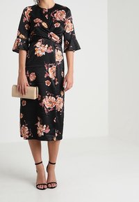 Černé květinové šaty s tříčtvrtečními rozšířenými rukávy, zdobené oranžovými a růžovými květy. Hladká látka, ke kolenům, doplněné béžovou psaníčkem.