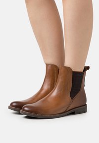 Brown leather ankle boots with elastic side panels, a rounded toe, and low stacked heel, featuring a smooth texture and minimal stitching.