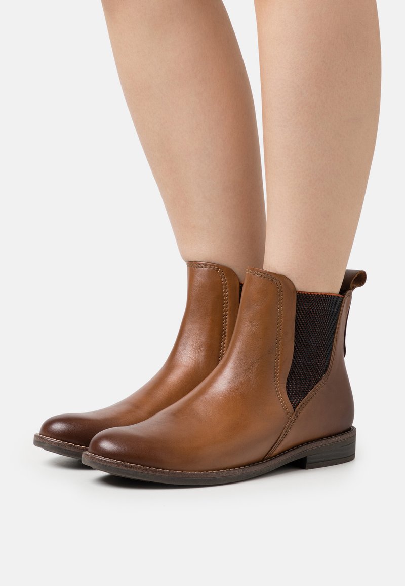 Brown leather ankle boots with elastic side panels, a rounded toe, and low stacked heel, featuring a smooth texture and minimal stitching.