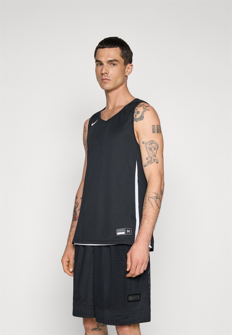 Top atletico senza maniche in rete nera con scollo a V, caratterizzato da una striscia laterale bianca e un'etichetta con logo sull'orlo. Indossato con pantaloni corti in rete neri.