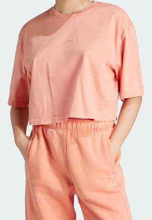 Przycięta różowa bawełniana koszulka z haftowanym logo Adidas, w połączeniu z pasującymi lekkimi różowymi dresami z elastycznym pasem i bocznymi kieszeniami.