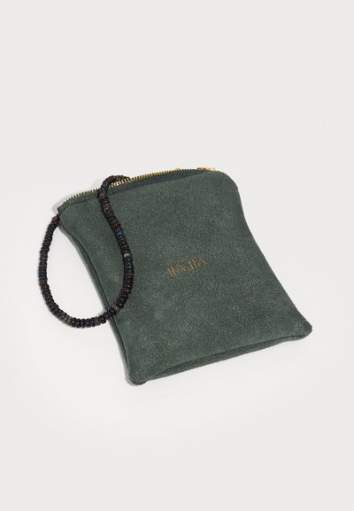 Σκούρο πράσινο σουέτ πουγκί με χρυσό φερμουάρ, χρυσό λογότυπο "JIAJIA" και μαύρη χαντρούλα στον καρπό που βρίσκεται σε λευκή επιφάνεια.