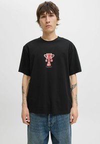 Sort bomulds T-shirt med et rødt grafik af en trofæ med teksten "1986" og "INTERNATIONAL". Korte ærmer og afslappet pasform. Blå jeans.