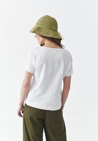 White short-sleeve t-shirt with a loose fit, paired with olive green wide-leg pants and a patterned olive green bucket hat.