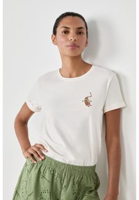 Camiseta corta de manga con vuelta en color crema, que presenta un gráfico estampado de temática veraniega en el pecho. Combinada con pantalones cortos verdes con textura.