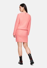 Rosa strukturierter Zweiteiler bestehend aus einem langärmeligen Oberteil und einem figurbetonten Rock, kombiniert mit kniefreien schwarzen und burgunderfarbenen Stiefeln.