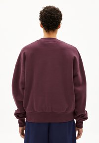 Burgunderfarbener Oversized-Pullover mit Rundhalsausschnitt, langen Ärmeln und gerippten Bündchen, der eine glatte, weiche Textur und eine lockere Passform bietet.