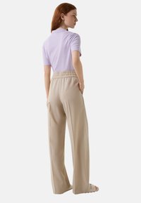Lichtpaarse polo met korte mouwen, gecombineerd met beige wijde broeken met een elastische tailleband en zijzakken. Soepele stoftextuur.