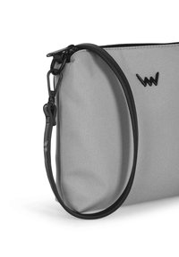 Šedá textilní taška s černým zipem a popruhem. Vyznačuje se elegantním designem a akcentem loga. Hladká textura s odolnými materiály.