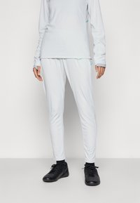 Set atletico grigio chiaro composto da una maglietta a maniche lunghe e pantaloni tapered, con dettagli turchesi e tessuto traspirante. Scarpe sportive nere.
