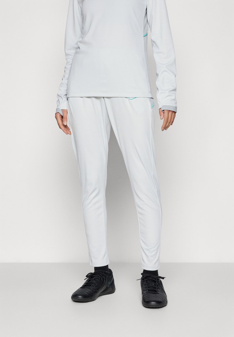 Set atletico grigio chiaro composto da una maglietta a maniche lunghe e pantaloni tapered, con dettagli turchesi e tessuto traspirante. Scarpe sportive nere.