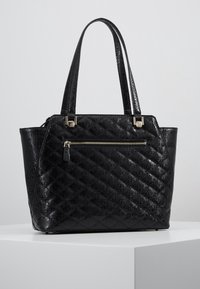 Sac fourre-tout en similicuir noir avec motif matelassé, poignées doubles et une poche zippée à l'avant avec ferrures argentées. Texture lisse sur toute la surface.