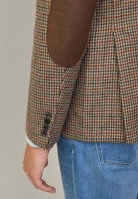 Houndstooth-muster brauner Tweed-Blazer mit braunen Wildleder-Ärmelflicken, ausgestattet mit einem Drei-Knopf-Bündchen und einer taillierten Passform.