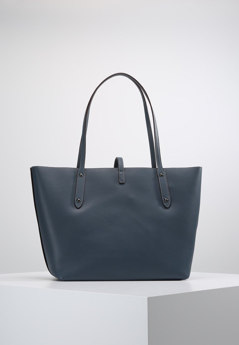 Bolso tote de cuero texturizado azul con dobles asas largas, fondo plano y una correa de cierre central. Presenta acentos suaves y herrajes metálicos.