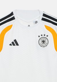 Biała sportowa koszulka z czarnymi, pomarańczowymi i szarymi akcentami, z czarnym logo Adidas i herbem Niemieckiego Związku Piłki Nożnej.