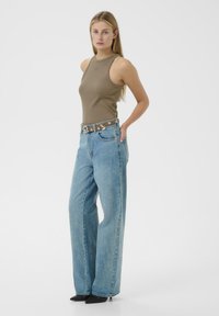 Barna ujjatlan felső, magas derekú világoskék bőszárú farmerrel párosítva, díszes övvel és hegyes fekete magassarkúval.