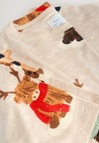 Mäkké béžové detské pyžamo s jeleňom, ktorý má na sebe červený šál, a malou nálepkou s nápisom "RODINNÝ" pri golieri.