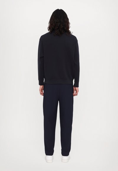 Sweatshirt marine et pantalon assorti en tissu doux. Le sweatshirt est doté d'un col rond et de poignets côtelés. Des baskets blanches complètent la tenue.